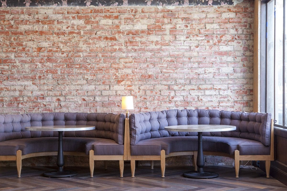 Cadet restaurant booth brick wall. Intérieur du restaurant Cadet, mur de briques. canapés mauves et tables.