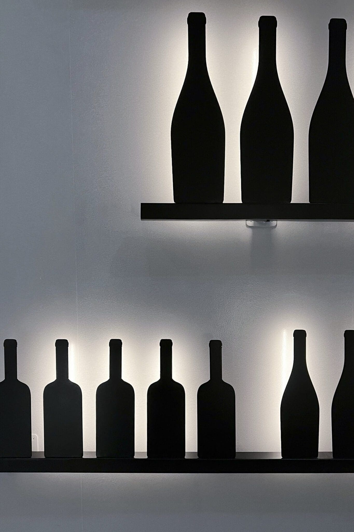 Zoom sur le mur dessiné par IchetKar, bouteilles et étagères en metal noir, rétro éclairées façon ombre chinoise